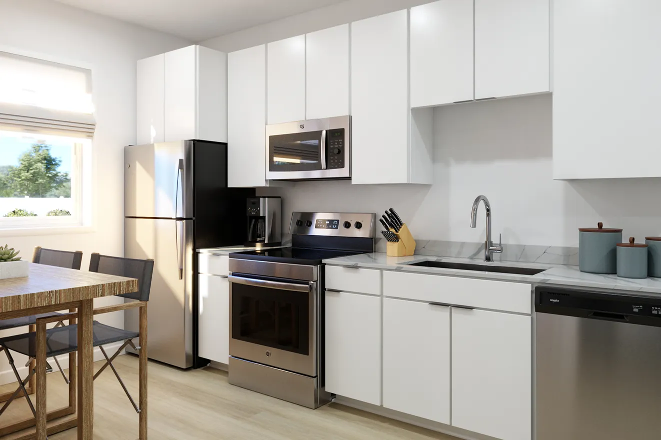 Modern kitchen with white cabinets, stainless steel appliances including fridge, stove, microwave, and dishwasher. A wooden table and chairs are near a sunny window.